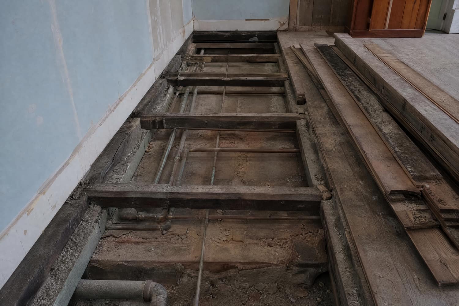 Pipe run replaced under a floor. Lifted floorboards showing old corroded copper pipe runs between joists.